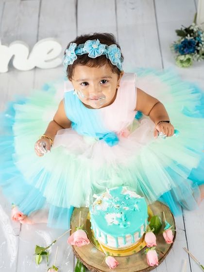 An aerial view of the birthday girl and her cake. This perspective shows off her gorgeous layered dress and the lovely details of the blue and pink floral setup.