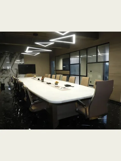 The main conference room, designed for formal meetings. It features a large central table, comfortable executive chairs, and striking geometric overhead lighting, creating a functional and impressive space.