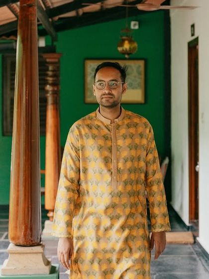 The groom, in a yellow printed kurta, walks along the verandah, a relaxed and handsome portrait.