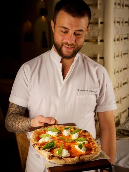 A chef proudly presenting his freshly baked pizza. Including the creator in the shot adds a human element and tells a story of passion and craftsmanship.