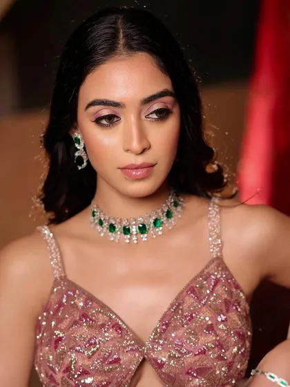 A close-up of this soft glam cocktail look. The focus is on the dazzling details, from the shimmery pink eyeshadow to the flawless skin that complements the emerald and diamond jewelry.