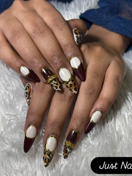 A fierce and fashionable design on long stiletto nails. This set combines deep burgundy, leopard print, and a bold white and gold accent for a high-fashion statement.