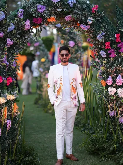 Here is one of my custom bandhgala jackets, seen at a beautiful garden wedding. The crisp white fabric is the canvas for a hand-painted floral and bird motif, designed to complement the festive atmosphere. This is how you make a statement with elegance.