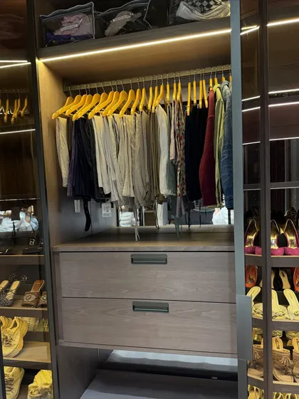 A glimpse into an organized closet, showing hanging trousers next to a beautifully arranged shoe and accessory display.