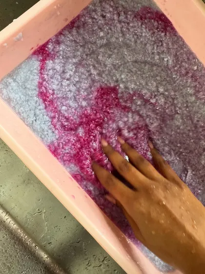Experimenting with adding natural dyes to my paper pulp. Here, I'm swirling in a beautiful magenta pigment to create colored, recycled paper sheets.