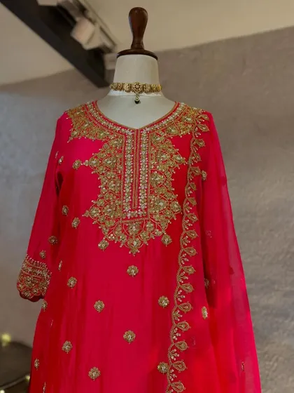 A close-up of the fuchsia pink suit, showcasing its rich gold embroidery on the neckline and sleeves, a truly regal piece.