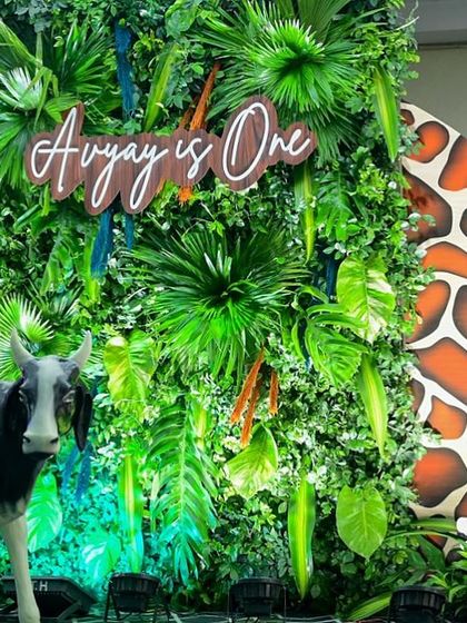 "Avyay is One!" For this jungle themed first birthday, we created a dense green wall of tropical leaves as a backdrop, complete with a custom wooden sign and fun animal props like this giraffe print accent.