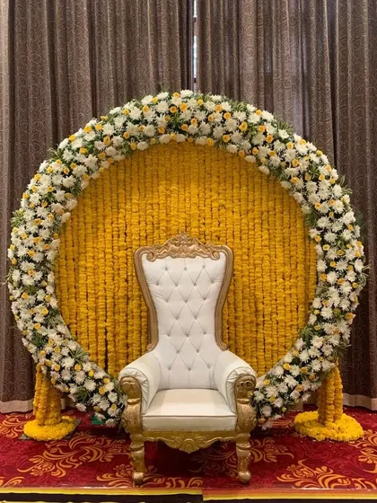 We bring vibrancy and tradition to your pre-wedding functions. This circular backdrop, made entirely of fresh marigold strings and bordered with white and yellow flowers, is a perfect, joyful setting for a Haldi or Mehendi ceremony.