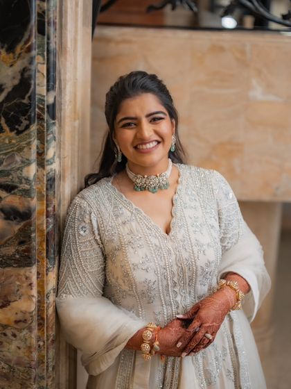 A beautiful close-up of the bride on her Sangeet night. Her smile lights up the frame, and you can see the exquisite detail of the zardozi work on her ivory outfit and her stunning emerald choker.