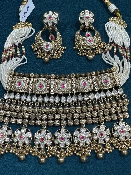 I love the craftsmanship on this antique finish choker set. The design has very detailed work with ruby-colored stones and is paired with beautiful chandbali earrings and delicate pearl strings, giving it a complete and traditional look.
