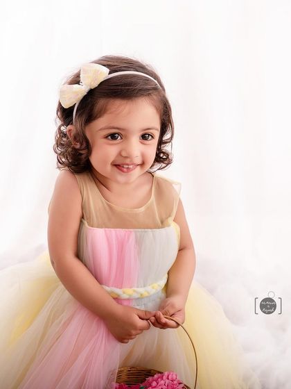 A sweet smile from this flower girl, dressed in a pastel rainbow gown and holding a basket of pink blossoms.