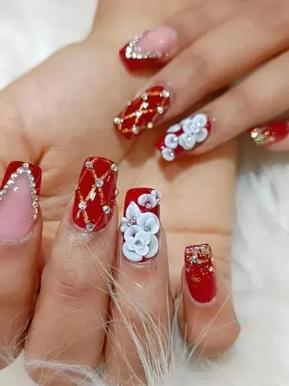 This is a perfect example of our detailed bridal nail art. The design features a rich red base with intricate rhinestone patterns, a quilted effect, and stunning 3D floral accents.