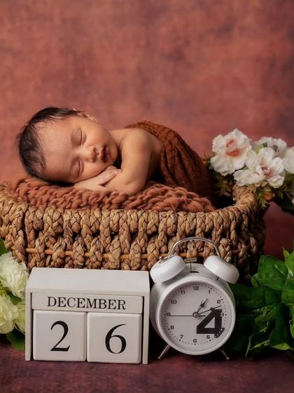A newborn sleeps in a woven basket next to a calendar block and clock, a perfect way to announce a birth date.