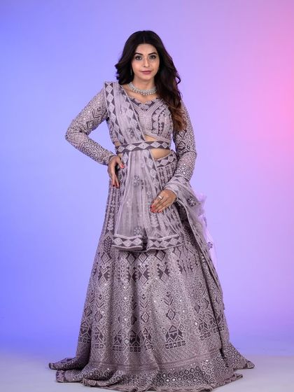 A full-length view of the lilac lehenga, showcasing its intricate geometric embroidery and mirror work. The belted dupatta adds a modern, cinched-in silhouette.