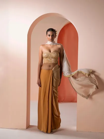 A contemporary take on the saree, featuring a gold embroidered bustier paired with a draped mustard-colored skirt and a flowing scarf.