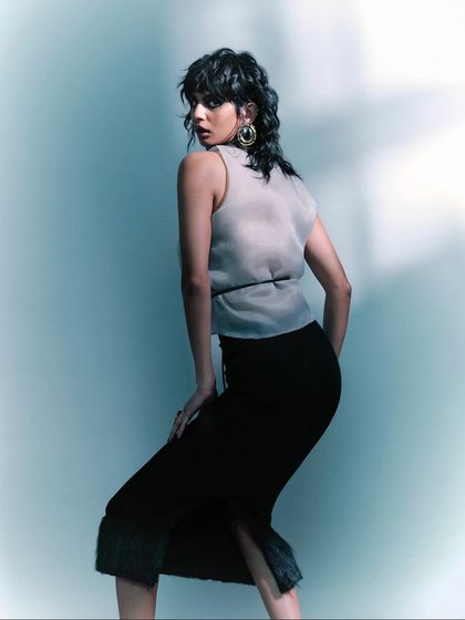 A three-quarter shot that highlights the texture of the sheer top and the model's dynamic pose. The styling is sophisticated and modern, perfect for a fashion editorial.