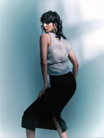A three-quarter shot that highlights the texture of the sheer top and the model's dynamic pose. The styling is sophisticated and modern, perfect for a fashion editorial.
