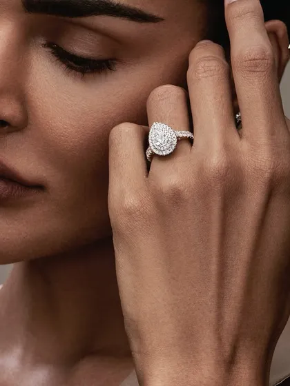 A detailed shot focusing on the hand and face for Aukera Jewellery. The makeup is minimal and skin-focused, with clean nails, ensuring the stunning pear-shaped diamond ring is the hero.