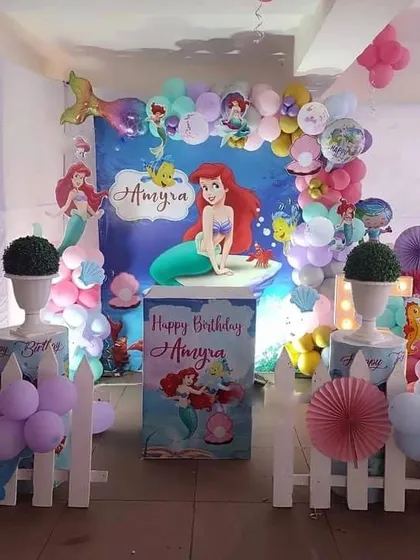 An underwater adventure with this Little Mermaid themed birthday party. The setup includes a character backdrop, a personalized cake stand, and a balloon arch in ocean colors.