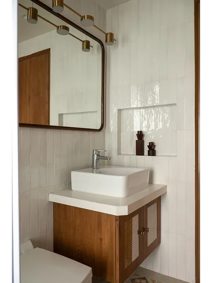 A simple yet elegant bathroom design, featuring a wood vanity, a large mirror with integrated lighting, and clean, white tiles. The design is minimalist but warm, focusing on functionality and quality materials.