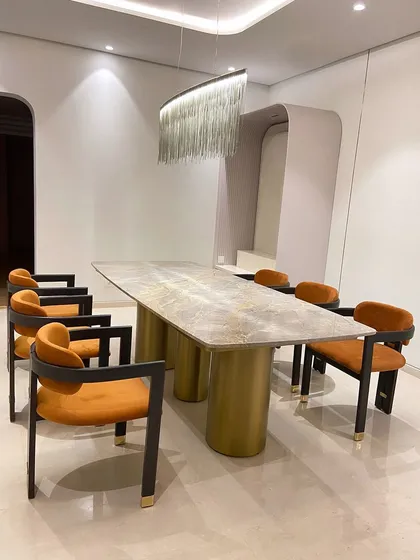 A bold statement in a client's dining room. We crafted this large dining table with a veined marble top and two substantial cylindrical metal legs, paired with vibrant orange velvet chairs.
