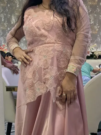 A decent and elegant pastel pink party wear gown with an asymmetrical floral overlay. This premium outfit is available to rent or buy.