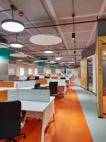 This workspace features bright orange flooring to define walkways and circulation paths. The use of color and circular meeting pods breaks the monotony of a traditional office layout.