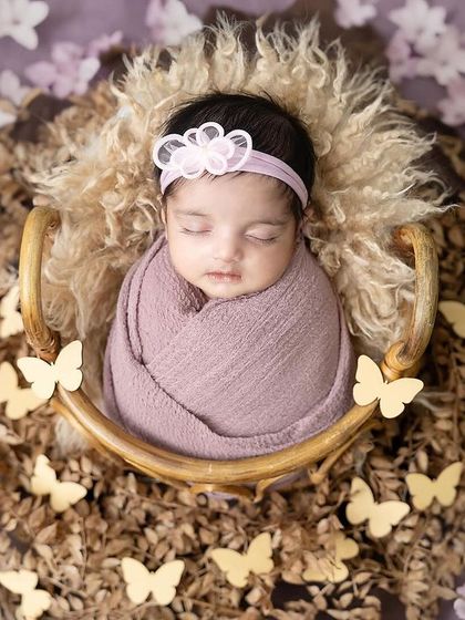 A butterfly dream. This newborn girl is sleeping in a rustic basket, surrounded by delicate paper butterflies for a whimsical touch.