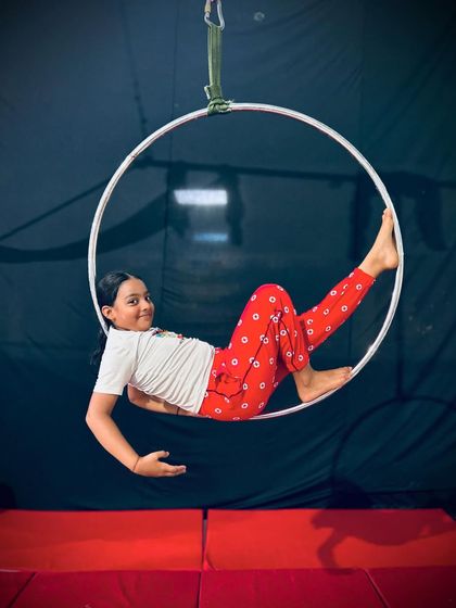 A young student smiles as she relaxes in the center of the aerial hoop, a simple and fun pose for beginners.