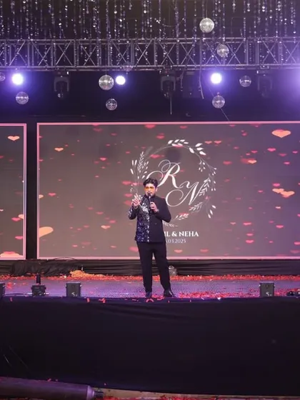 On stage with a large screen backdrop, commanding the attention of the audience. A professional emcee needs to have a strong stage presence to manage large-scale productions and keep the event flowing smoothly.