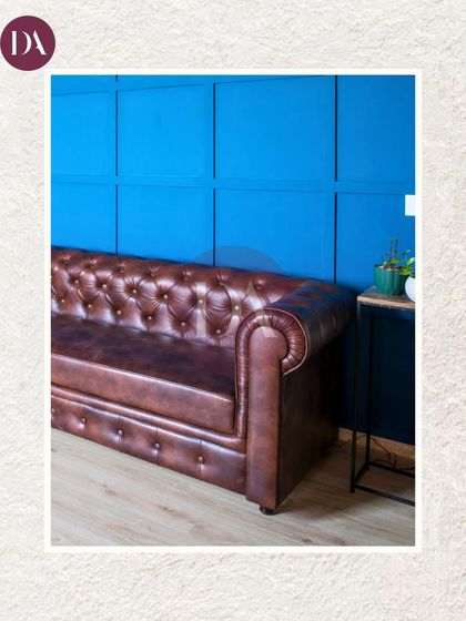 A detail shot of a classic brown Chesterfield sofa against a vibrant blue paneled wall. This image captures our belief that every corner should tell a story and breathe soul.