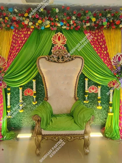A grand decoration for a Simmanta or Godh Bharai ceremony, with a large ornate chair, a green grass wall, and colorful fabric drapes.