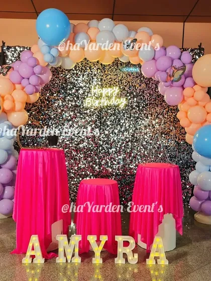 A beautiful pastel-colored balloon arch over a silver sequin backdrop. This setup, with its pink draped tables, is perfect for a sweet 16 or a stylish birthday brunch.