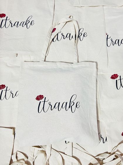 A closer look at the elegant 'itraake' tote bag. The combination of a delicate script and a small floral detail creates a sophisticated look on this natural cotton bag, perfect for fashion and lifestyle brands.