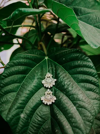 A creative detail shot of the bride's earrings resting on a large green leaf, connecting the elegance of the jewelry with the natural beauty of the wedding location.