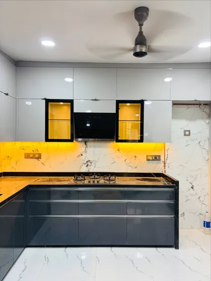 This is a modern modular kitchen I designed, featuring a sleek two-tone look with glossy grey and white cabinets. I used under-cabinet LED lighting to illuminate the marble-patterned backsplash and black granite countertop, creating a workspace that is both stylish and practical.