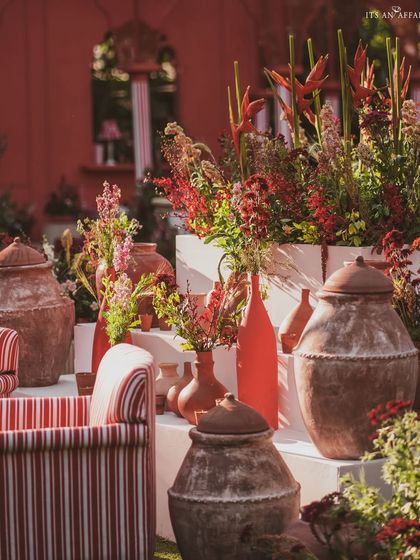 A collection of terracotta pots and vibrant red floral arrangements adds a rustic and earthy element to the 'Gulal Bagh' decor.