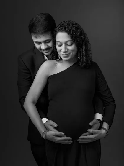 An intimate black and white portrait, with the father-to-be's hands gently placed over his wife's on the baby bump, symbolizing their shared journey.