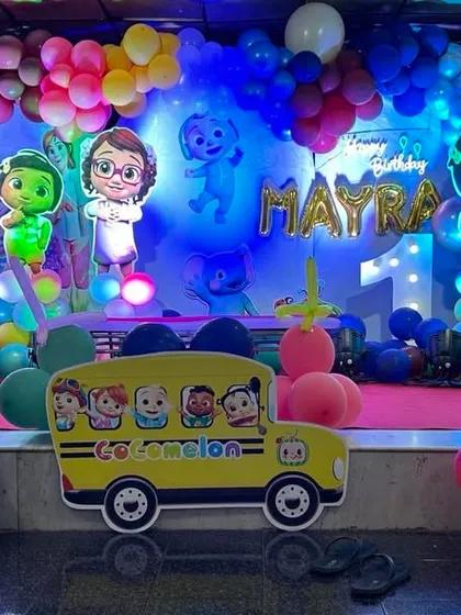 A complete stage setup for a Cocomelon first birthday party. I filled the stage with colorful balloon garlands and life-sized cutouts of JJ and his friends, with the iconic yellow school bus right at the front.