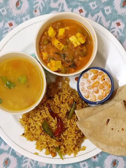 A plated version of one of my popular meals: Puliyogre rice, mutter paneer, dal, and boondi raita, served with soft rotis.