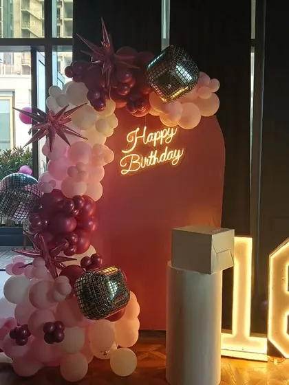 A sweet 16 birthday party with a pink arched backdrop. The decoration includes a balloon garland with disco balls and starburst accents, a neon sign, and a marquee number '16'.