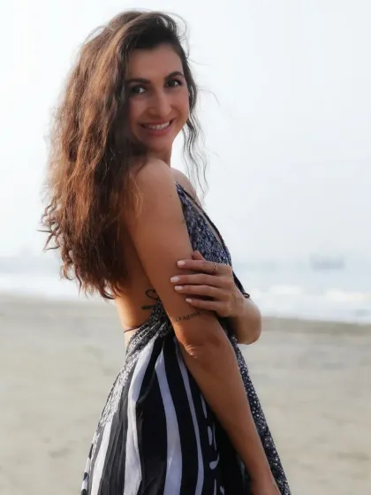 A warm, friendly portrait of a woman on the beach, looking back at the camera with a gentle smile.