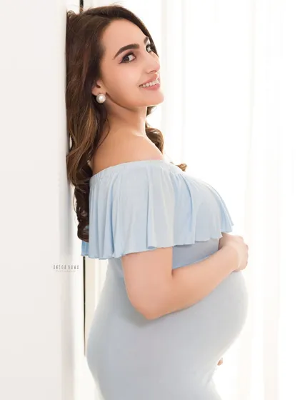 A simple and elegant pose against a white wall. The clean background and soft light put all the focus on the mother's happy expression and beautiful baby bump.