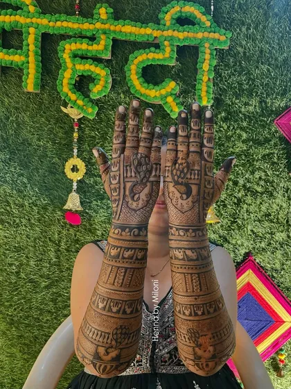 A happy bride showing her full bridal mehendi against the backdrop of her mehendi ceremony decor.