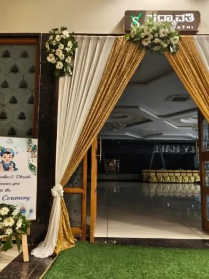 An elegant entrance for a Naming Ceremony. The doorway is framed with white and sequined gold drapes, and a custom welcome sign featuring a Little Krishna theme greets the guests.