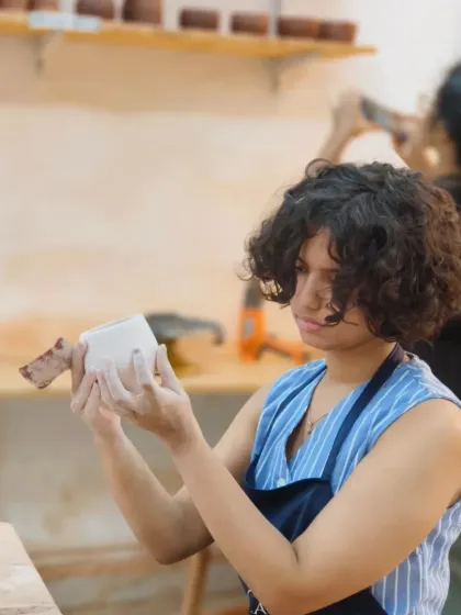 A student carefully inspects her hand-built mug, checking the form and the attachment of the handle. This attention to detail is a key part of the creation process we teach.