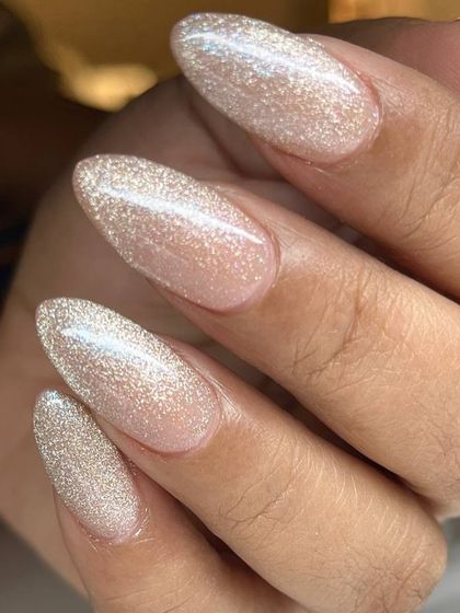 A beautiful, shimmery champagne-gold polish on long, almond-shaped nails. The finish is somewhere between a glitter and a cat-eye, creating a unique, velvety sparkle.