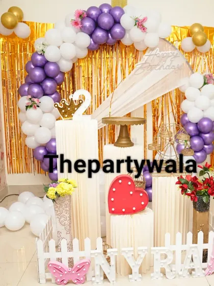 A beautiful ring decoration with a purple and white balloon arch against a gold shimmer backdrop. The picket fence and props add a charming touch.