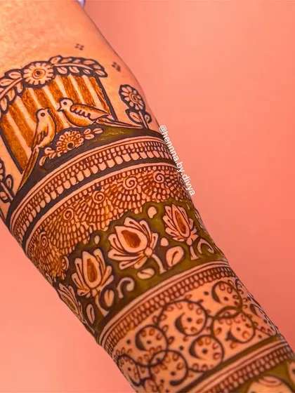 A close-up of a forearm band featuring two love birds perched in a cage. This romantic detail is part of a larger bridal design, adding a sweet, personal touch.