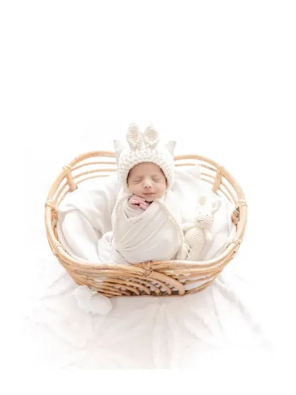 A newborn wearing an adorable bunny hat sleeps in a rustic wicker basket. This classic newborn portrait is simple, sweet, and timeless, focusing on the baby's peaceful expression and tiny features.